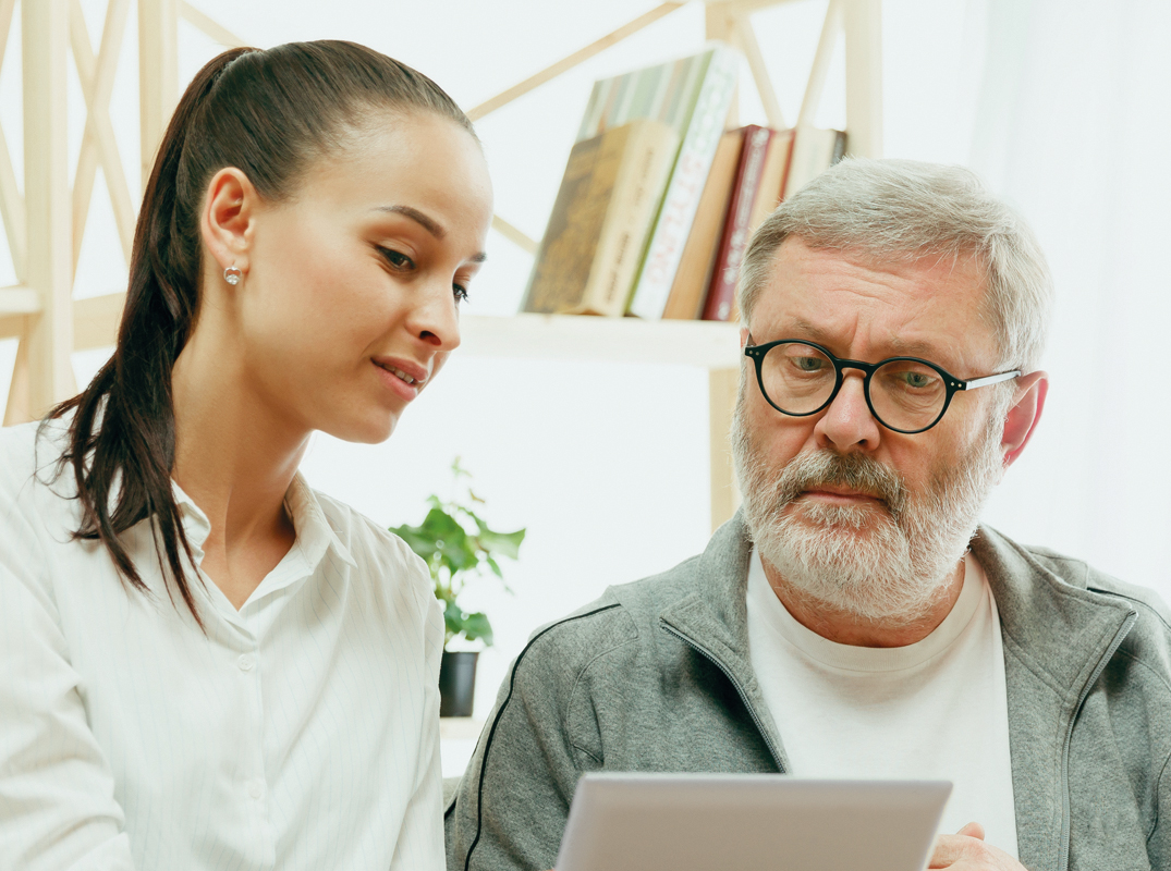 Unsere Therapieangebote für Erwachsene, Bild von einem älteren Herren und einer jungen Dame, die gemeinsam auf einen Laptop schauen.