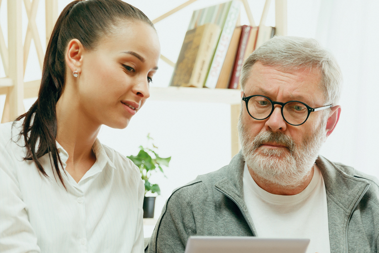 Therapieangebote für Erwachsene, Bild von einem älterem Herrn mit weißem Haar, Bart und Brille und einer jungen Dame mit schwarzem Haar. Beide schauen auf einen Laptop Bildschirm